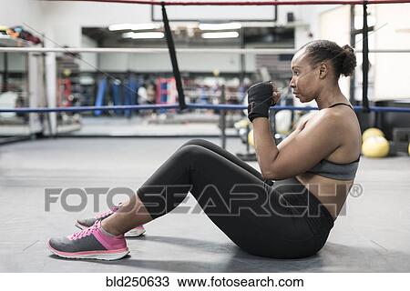 Stock Image - Black woman sitting on floor in boxing ring. Fotosearch