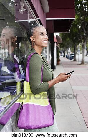 Stock Image - Black woman text messaging on sidewalk. Fotosearch