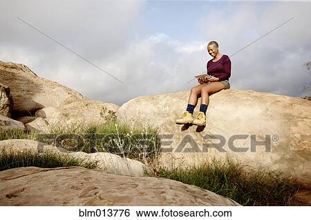 Stock Photograph - Black woman using digital tablet on rock. Fotosearch