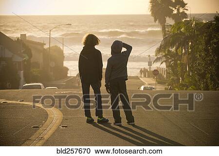 Stock Image - Boys standing in street admiring ocean waves. Fotosearch