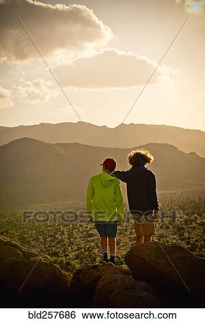 Stock Photograph - Boys standing on rock admiring desert landscape. Fotosearch