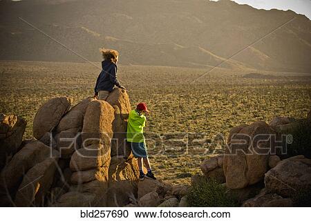 Stock Image - Boys standing on rocks admiring desert landscape. Fotosearch