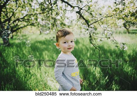 Stock Photography - Bubbles floating near Caucasian boy in field near tree. Fotosearch