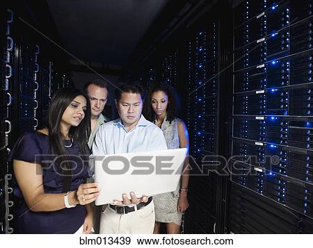 Stock Photo - Business people looking at laptop in server room. Fotosearch