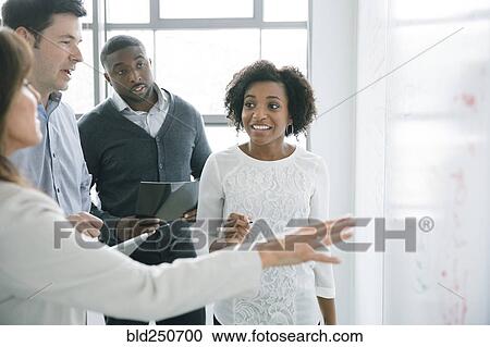 Stock Image - Business people talking near whiteboard in meeting. Fotosearch