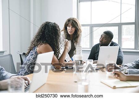 Stock Image - Business people using laptop in meeting. Fotosearch