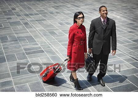 Stock Image - Business people with briefcase and rolling suitcase. Fotosearch