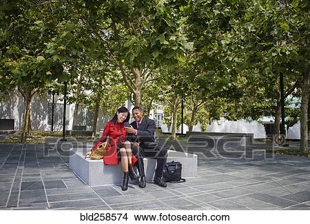 Picture - Businessman showing cell phone to businesswoman at park. Fotosearch