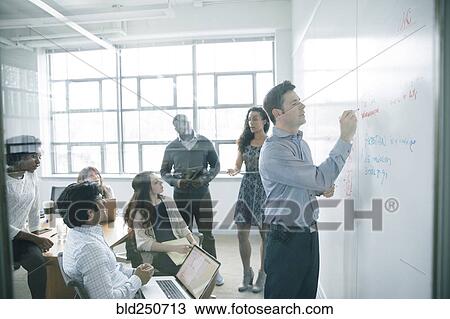 Stock Image - Businessman writing on whiteboard in meeting. Fotosearch