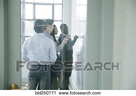 Stock Image - Businessman writing on whiteboard in meeting behind window. Fotosearch