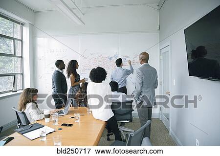 Stock Photo - Businessman writing on whiteboard in meeting. Fotosearch