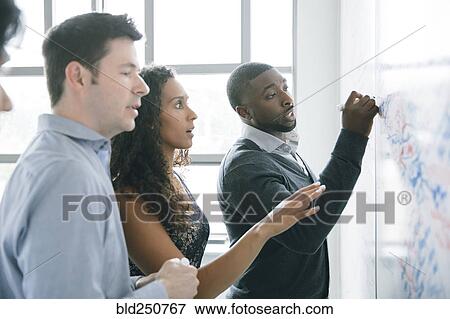 Stock Photo - Businessman writing on whiteboard in meeting. Fotosearch