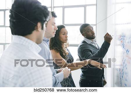 Stock Photo - Businessman writing on whiteboard in meeting. Fotosearch