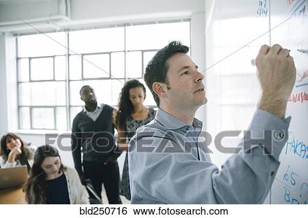 Stock Photograph - Businessman writing on whiteboard in meeting. Fotosearch