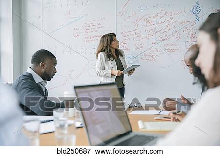 Businesswoman holding digital tablet near whiteboard in meeting View Large Photo Image Stock Photo - Businesswoman holding digital tablet near whiteboard in meeting. Fotosearch
