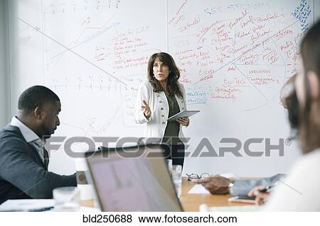 Businesswoman holding digital tablet near whiteboard in meeting View Large Photo Image Stock Photo - Businesswoman holding digital tablet near whiteboard in meeting. Fotosearch