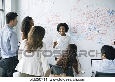 Stock Image - Businesswoman talking near whiteboard in meeting. Fotosearch