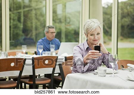Stock Image - Businesswoman texting on cell phone in restaurant. Fotosearch