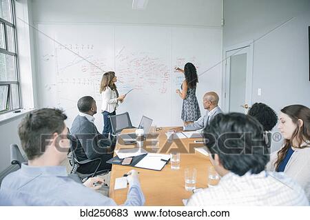 Stock Image - Businesswoman writing on whiteboard in meeting. Fotosearch