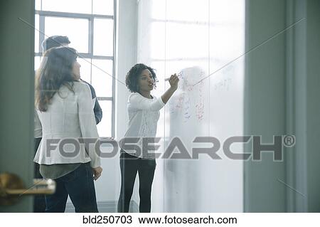 Stock Image - Businesswoman writing on whiteboard in meeting. Fotosearch