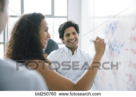 Stock Image - Businesswoman writing on whiteboard in meeting. Fotosearch