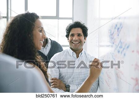 Stock Image - Businesswoman writing on whiteboard in meeting. Fotosearch
