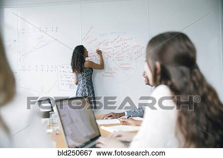 Stock Photo - Businesswoman writing on whiteboard in meeting. Fotosearch