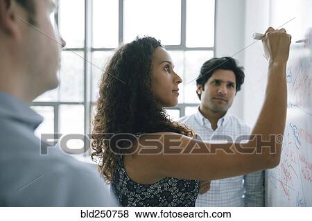 Stock Photo - Businesswoman writing on whiteboard in meeting. Fotosearch