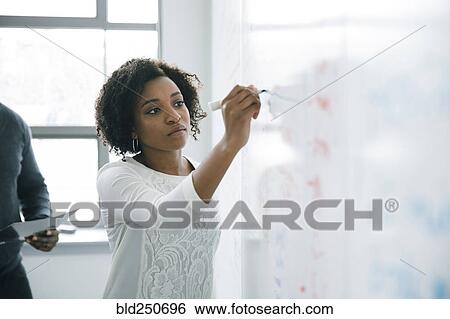 Stock Photograph - Businesswoman writing on whiteboard in meeting. Fotosearch