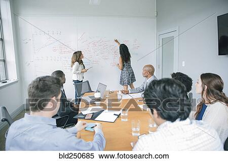 Stock Photography - Businesswoman writing on whiteboard in meeting. Fotosearch