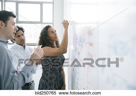Stock Photography - Businesswoman writing on whiteboard in meeting. Fotosearch