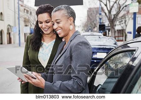 Stock Image - Businesswomen looking at digital tablet outdoors. Fotosearch