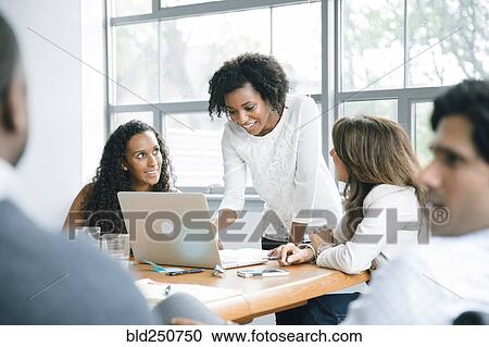Stock Image - Businesswomen using laptop in meeting. Fotosearch