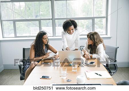 Stock Image - Businesswomen using laptop in meeting. Fotosearch