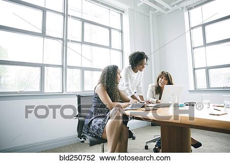 Stock Image - Businesswomen using laptop in meeting. Fotosearch