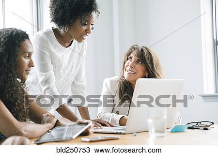 Stock Image - Businesswomen using laptop in meeting. Fotosearch