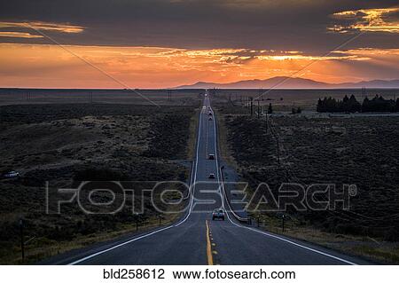 Stock Image - Cars driving on remote road at sunset. Fotosearch
