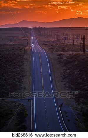 Stock Photograph - Cars driving on remote road at sunset. Fotosearch
