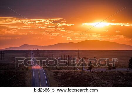 Stock Photography - Cars driving on remote road at sunset. Fotosearch