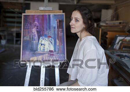 Stock Photograph - Caucasian artist sitting near paintings. Fotosearch