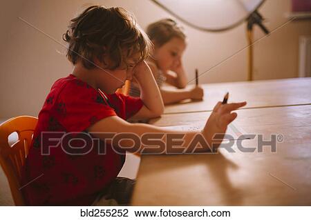 Stock Image - Caucasian boy and girl sitting at table with pencil and paper. Fotosearch