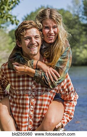 Stock Image - Caucasian boy carrying girl piggyback at river. Fotosearch