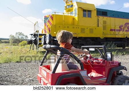 Stock Image - Caucasian boy driving toy car near train. Fotosearch