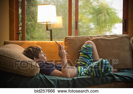 Caucasian boy laying on sofa texting on cell phone View Large Photo Image Stock Photograph - Caucasian boy laying on sofa texting on cell phone. Fotosearch