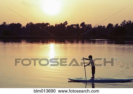 Stock Image - Caucasian boy on paddleboard on lake. Fotosearch
