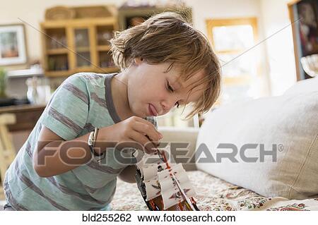Stock Image - Caucasian boy playing with toy boat on sofa. Fotosearch