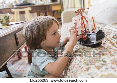 Stock Image - Caucasian boy playing with toy boat on sofa. Fotosearch