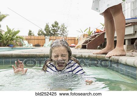 Stock Photography - Caucasian boy pouring water on sister in swimming pool. Fotosearch