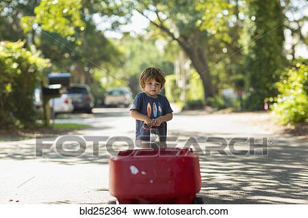 Picture - Caucasian boy pulling red wagon in street. Fotosearch