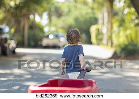 Stock Photo - Caucasian boy pulling red wagon in street. Fotosearch